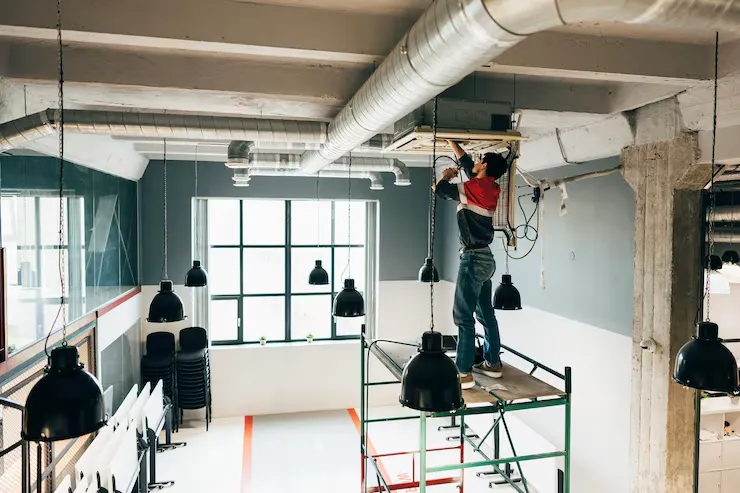 A technician working on low-voltage network cabling and wiring near an open commercial office ceiling.